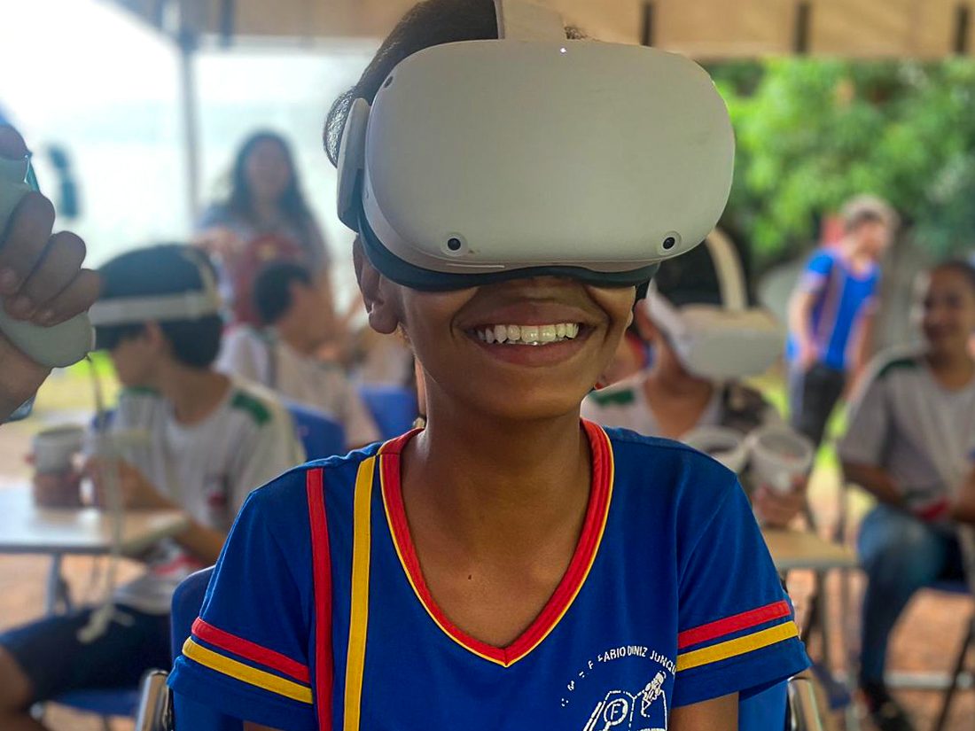 Estudante de escola pública sorri usando óculos de realidade virtual no circuito MT Ciências