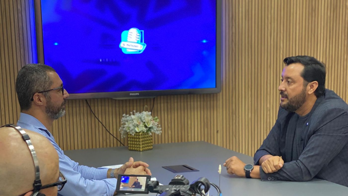 Allan Kardec concede entrevista em estúdio de televisão, com câmera e telão em quadro